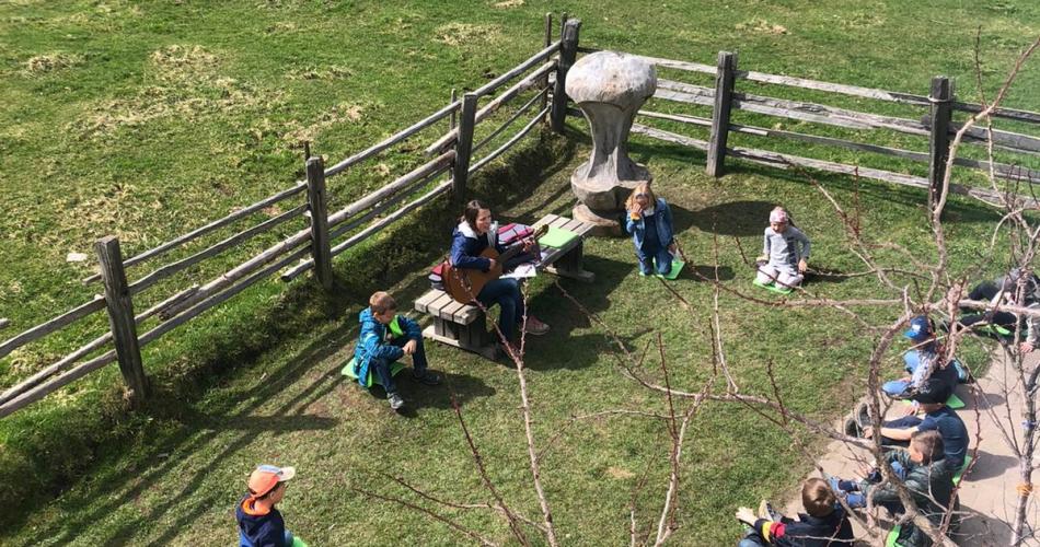 Kinder sitzen hinter dem Schulhaus im Freien